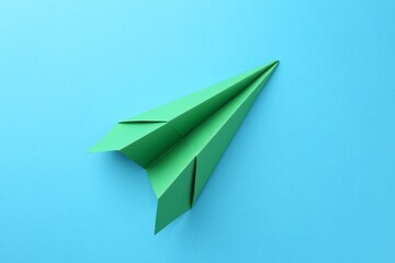 Naklejka premium One handmade green paper plane on light blue background, top view