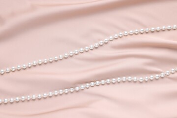 Elegant pearl necklace on beige fabric, top view