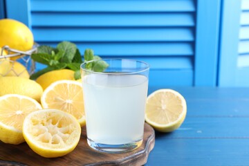 Fresh juice in glass, lemons and mint on blue wooden table. Space for text