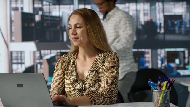 Confident skilled entrepreneur seated at her corporate office desk, is deep in her thoughts using laptop to forecast business growth. Managing financial planning and achieving goals. Camera A.