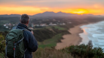 Naklejka premium Man with Backpack Capturing Sunset Over Beach and Mountains