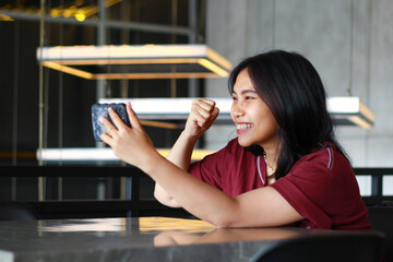 pretty and attractive asian woman raised fist celebrating winning playing game online using smartphone in cafe