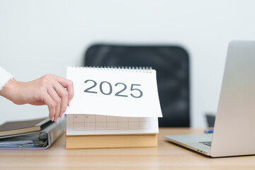 Business woman change 2025 Year Calendar on table with laptop computer during working and writing...