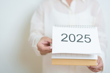 Business woman hand holding and change 2025 Year Calendar on white background table in office. countdown, Happy New Year, Resolution, Year End and New Start and Goals Plan Action Concept