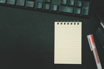 Top view of notebook. Blank paper notepad on office desk table with keyboard and other supplies....