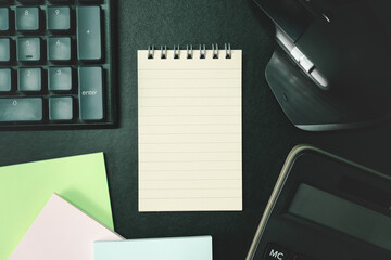 Top view of notebook. Blank paper notepad on office desk table with keyboard and other supplies....