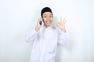 smiling muslim asian man show okay sign while talking on his phone with smiling face isolated