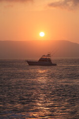 Obraz premium Beach sunrise: orange sky, calm sea, boat, captivating beauty in nature.
