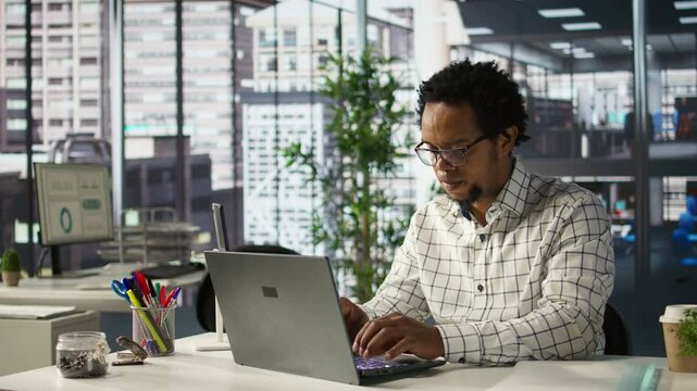 African american general manager reviews business forecasts and plans on his laptop at office desk, strategy planning. Data analyst focuses on company objectives and resource allocation. Camera B.