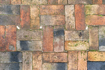 Ancient red brick flooring on an outdoor sidewalk, featuring a woven texture or abstract design.