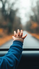 A child's hand reaches out from a car window, touching the glass as a blurred autumn landscape unfolds beyond.