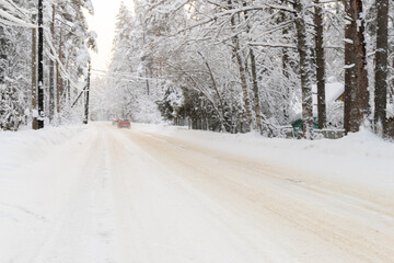 Snowy road in winter forest with driving cars in a distance. Pine trees and spruce peaceful landscape on countryside. Snowfall. Serenity scene.
