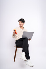 Full body image of a young businessman sitting in a chair  , using laptop , phone and posing on a white background