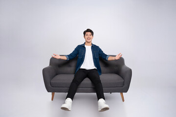 Full body image of young Asian man posing on sofa on white background