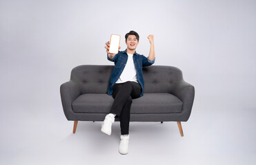 Full body image of young Asian man using phone sitting on sofa on white background