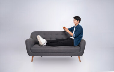 Full body image of young Asian man using phone sitting on sofa on white background