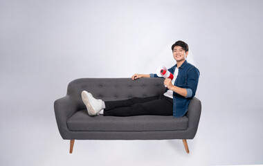 Full body image of young Asian man using hand speaker sitting on sofa on white background