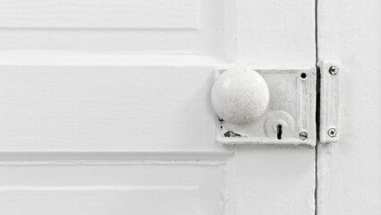 Close-up photo of an antique doorknob and lock with white chipped paint on an old wooden door with...