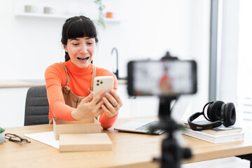 Caucasian female blogger enthusiastically unboxing new smartphone. Video recording setup with...