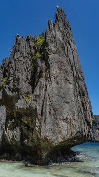 A picturesque karst rock against a background of blue sky and turquoise ocean. There is scant green vegetation on the steep furrowed slopes. Philippines. Palawan. The Secret lagoon. Bacuit Bay