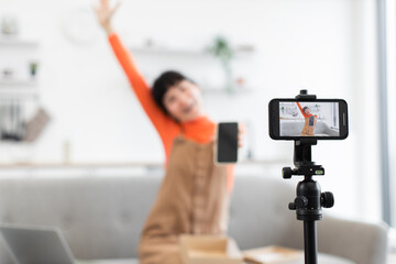 Fototapeta premium Caucasian female vlogger enthusiastically unboxing smartphone in front of camera. Young woman showcasing new gadget while sitting on sofa.
