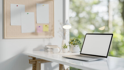 A close-up of a laptop on a white table by the window in a minimalist white office.