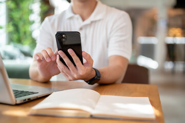 A man is reading chat messages on his smartphone while working remotely from a coffee shop.