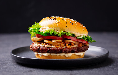 Burger with beef, cheese, vegetables on black plate. Dark Background. Close up.