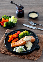 Salmon steak and herbs in black plate on table background.