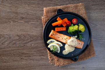 Salmon steak and herbs in black plate on table background.