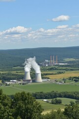 Nuclear Power Plant with Three White Towers Emitting Steam Surrounded by Green Fields and Trees