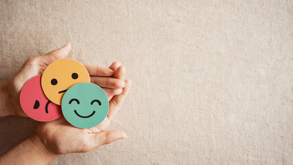 Hands holding sad face hiding behind happy face, psychology and mental health, emotional...