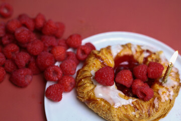 Delicious sweet pastry with raspberry and candles on the white plate and red background 