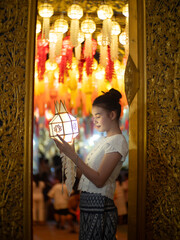 Beautiful Asian women holding a traditional paper lantern during Yi peng lantern festival at Wat Phra That Hariphunchai, Lamphun province, Thailand.