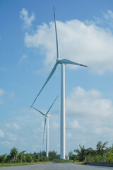 A large wind turbine for generating electricity using the force of the wind installed in an agricultural field against a blue sky.