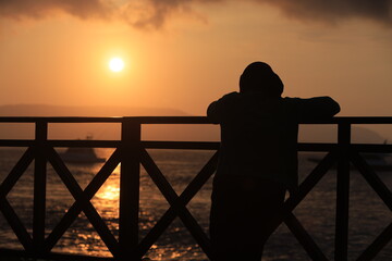 Obraz premium Silhouette figure at sunset on a calm beach with , bridge and ocean.