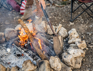 Campfire with person using a shovel to adjust logs and rocks