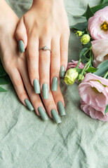 Elegant hands with green nail polish resting on a soft fabric surrounded by delicate flowers in a tranquil setting