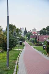 Fototapeta premium street scene in a small European town. The street is paved with cobblestones, and a central pedestrian island is visible, featuring benches and young trees.