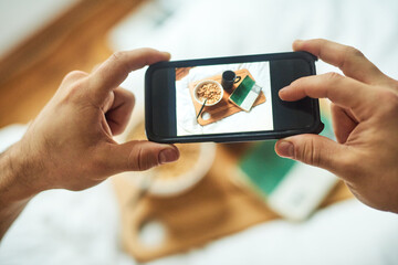Hands, phone and screen in bed for breakfast, photography or relax on weekend break with nutrition. Male person, mobile and food in home for social media app, top view or chill with coffee in morning