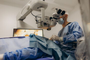 A surgeon looks through a microscope in the operating room. A doctor uses a microscope during eye...
