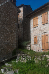 Uno scorcio del borgo di Erto presso la diga del Vajont con delle case dalle finestre chiuse e la strada coperta dall’erba verde