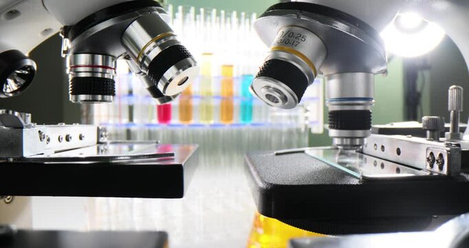 Microscope row focused on glass slides with colored liquid test tubes in background