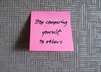 Pink note stick on wall with handwritten text - Stop comparing yourself to others - concept of awareness to negative effects of the comparison trap which leads to negative and anxious thoughts
