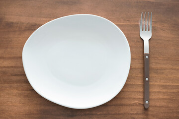 Empty white plate and fork on wooden background close-up top view.
