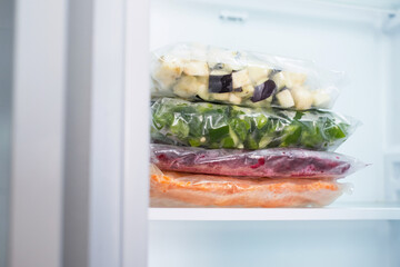 Stack of bags with chopped and frozen vegetables in refrigerator close-up.