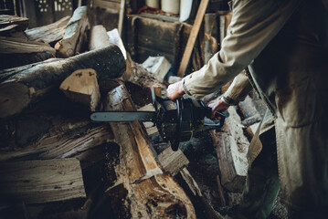 Old man in trench coat cutting firewood with a chainsaw.