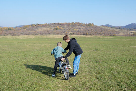 Older brother teaches younger to ride a bicycle, field and mountains