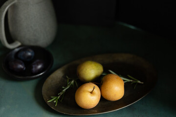 Artistic still life with pears, rosemary, plums, and a ceramic pitcher