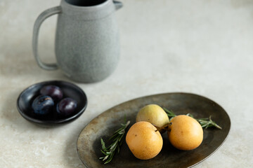 Minimalist still life with pears, plums, rosemary, and ceramic pitcher
